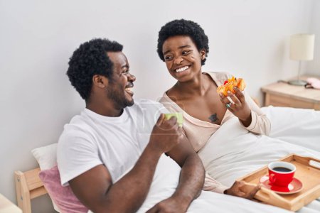 Photo for African american man and woman couple having breakfast sitting on bed at bedroom - Royalty Free Image