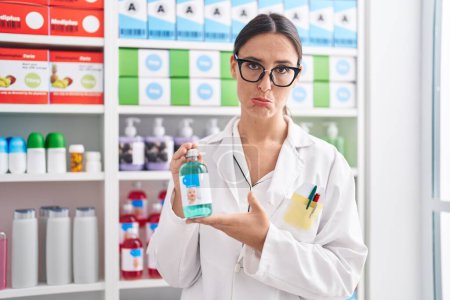 Photo for Brunette woman working at pharmacy drugstore holding cough syrup depressed and worry for distress, crying angry and afraid. sad expression. - Royalty Free Image