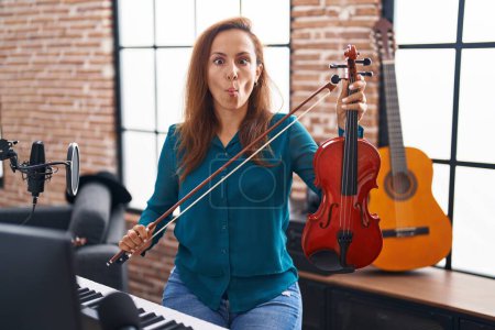 Photo for Brunette woman playing violin making fish face with mouth and squinting eyes, crazy and comical. - Royalty Free Image