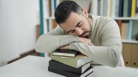 Photo for Young hispanic man student sleeping with head on books at library university - Royalty Free Image