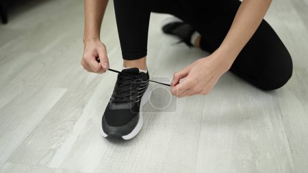 Photo for Young beautiful hispanic woman tying shoe at sport center - Royalty Free Image