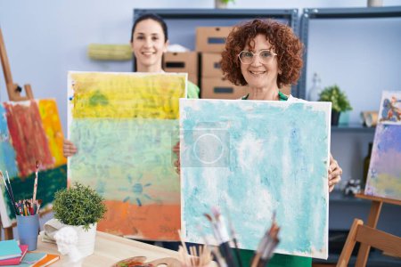 Téléchargez les photos : Deux femmes artistes souriantes confiantes tenant dessin sur toile au studio d'art - en image libre de droit