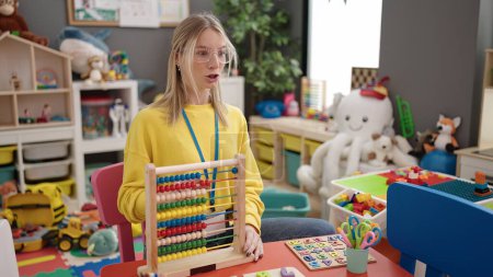 Photo for Young blonde woman working as teacher teaching maths with abacus at kindergarten - Royalty Free Image