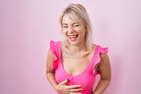 Téléchargez les photos : Jeune femme caucasienne debout sur fond rose souriant et riant fort à haute voix parce que drôle blague folle avec les mains sur le corps. - en image libre de droit