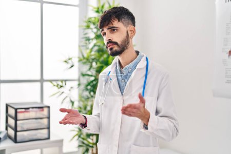 Téléchargez les photos : Jeune homme hispanique portant l'uniforme de médecin parlant à la clinique - en image libre de droit