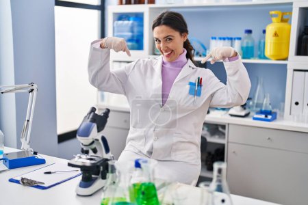 Photo for Young brunette woman working at scientist laboratory looking confident with smile on face, pointing oneself with fingers proud and happy. - Royalty Free Image