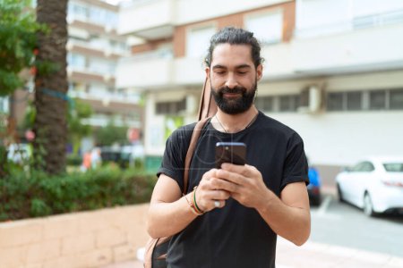 Téléchargez les photos : Jeune musicien hispanique utilisant un smartphone tenant un étui de guitare au parc - en image libre de droit