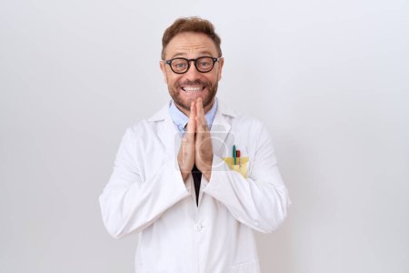 Photo for Middle age doctor man with beard wearing white coat praying with hands together asking for forgiveness smiling confident. - Royalty Free Image