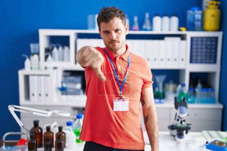 Photo for Young hispanic man working at scientist laboratory looking unhappy and angry showing rejection and negative with thumbs down gesture. bad expression. - Royalty Free Image