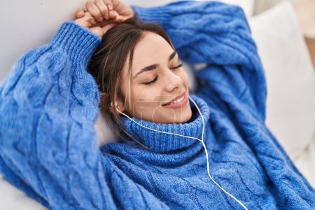 Téléchargez les photos : Jeune belle femme hispanique écoutant de la musique allongée sur le lit dans la chambre - en image libre de droit