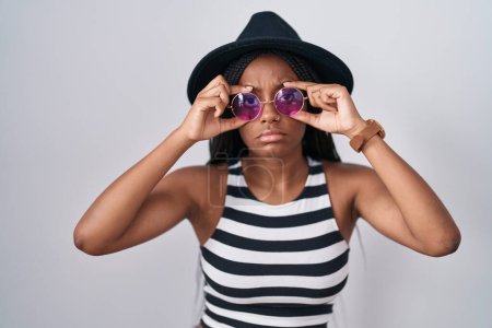 Photo for Young african american with braids wearing hat and sunglasses trying to open eyes with fingers, sleepy and tired for morning fatigue - Royalty Free Image