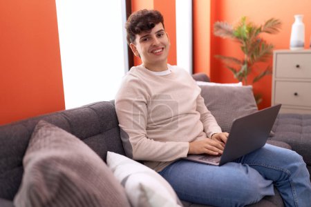 Photo for Non binary man using laptop sitting on sofa at home - Royalty Free Image
