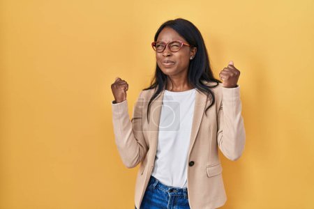Foto de Mujer joven africana con gafas muy contenta y emocionada haciendo gesto ganador con los brazos levantados, sonriendo y gritando por el éxito. concepto de celebración. - Imagen libre de derechos