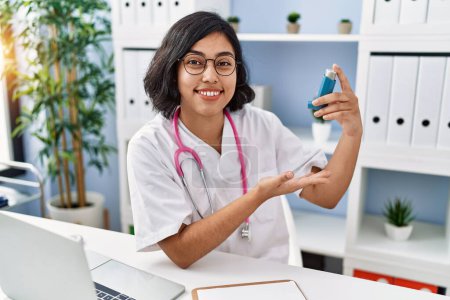 Photo for Young latin woman wearing doctor uniform holding inhaler at clinic - Royalty Free Image