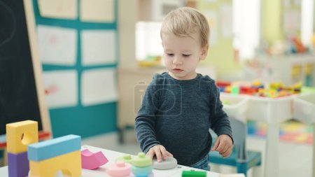 Foto de Adorable niño rubio jugando con bloques de geometría de pie en el jardín de infantes - Imagen libre de derechos