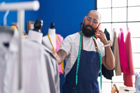 Téléchargez les photos : Jeune homme chauve tailleur parler sur smartphone regarder veste à l'usine de vêtements - en image libre de droit