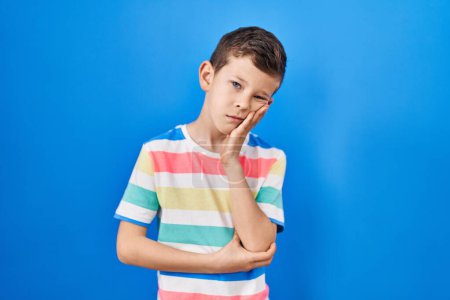 Photo for Young caucasian kid standing over blue background thinking looking tired and bored with depression problems with crossed arms. - Royalty Free Image
