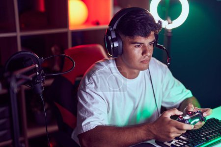 Foto de Young hispanic man streamer playing video game using joystick at gaming room - Imagen libre de derechos