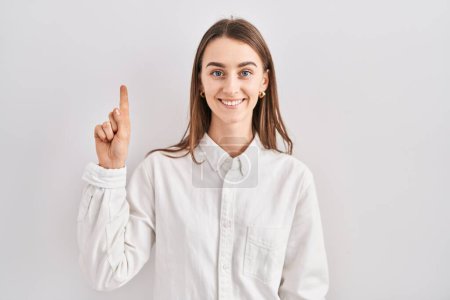 Photo for Young caucasian woman standing over isolated background showing and pointing up with finger number one while smiling confident and happy. - Royalty Free Image