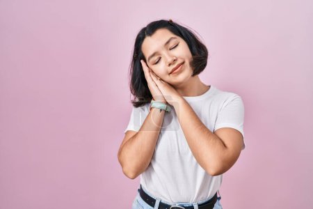 Photo for Young hispanic woman wearing casual white t shirt over pink background sleeping tired dreaming and posing with hands together while smiling with closed eyes. - Royalty Free Image