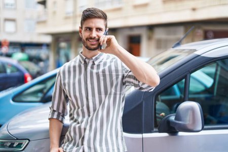 Photo for Young caucasian man talking on smartphone leaning on car at street - Royalty Free Image
