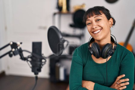 Téléchargez les photos : Jeune belle musicienne hispanique souriante confiante assise avec les bras croisés geste au studio de musique - en image libre de droit