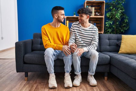 Téléchargez les photos : Couple de deux hommes assis sur le canapé avec les mains ensemble à la maison - en image libre de droit