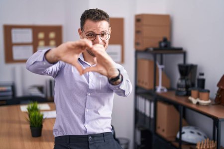 Photo for Young hispanic man at the office smiling in love doing heart symbol shape with hands. romantic concept. - Royalty Free Image