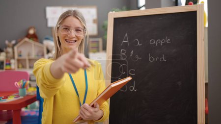 Photo for Young blonde woman preschool teacher pointing to camera at kindergarten - Royalty Free Image