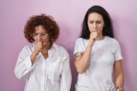 Photo for Hispanic mother and daughter wearing casual white t shirt over pink background feeling unwell and coughing as symptom for cold or bronchitis. health care concept. - Royalty Free Image