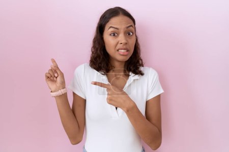 Photo for Young hispanic woman wearing casual white t shirt pointing aside worried and nervous with both hands, concerned and surprised expression - Royalty Free Image