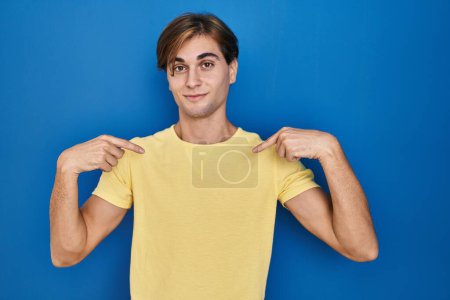 Photo for Young man standing over blue background looking confident with smile on face, pointing oneself with fingers proud and happy. - Royalty Free Image