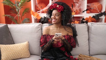 Téléchargez les photos : Femme afro-américaine portant un costume de katrina en utilisant un smartphone à la maison - en image libre de droit