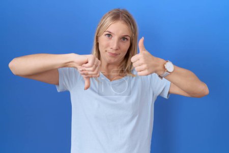Foto de Mujer caucásica joven con camiseta azul casual haciendo pulgares arriba y abajo, desacuerdo y expresión de acuerdo. conflicto loco - Imagen libre de derechos