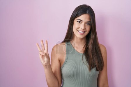 Téléchargez les photos : Hispanic woman standing over pink background showing and pointing up with fingers number three while smiling confident and happy. - en image libre de droit