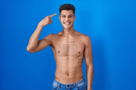 Photo for Young hispanic man standing shirtless over blue background smiling pointing to head with one finger, great idea or thought, good memory - Royalty Free Image