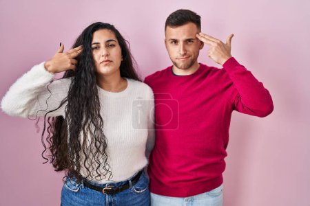 Téléchargez les photos : Young hispanic couple standing over pink background shooting and killing oneself pointing hand and fingers to head like gun, suicide gesture. - en image libre de droit