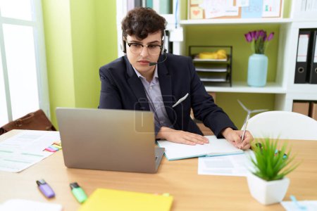 Foto de Hombre no binario agente de centro de llamadas utilizando la escritura de computadoras en el portátil en la oficina - Imagen libre de derechos