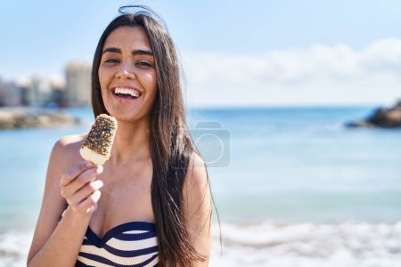 Photo for Young hispanic woman wearing bikini eating ice cream at seaside - Royalty Free Image