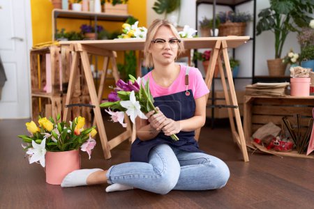 Photo for Young caucasian woman working at florist shop sitting of floor clueless and confused expression. doubt concept. - Royalty Free Image