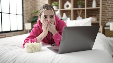Téléchargez les photos : Jeune femme blonde regardant un film allongé sur le lit dans la chambre - en image libre de droit