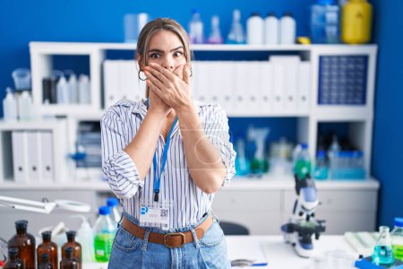 Photo for Young beautiful woman working at scientist laboratory shocked covering mouth with hands for mistake. secret concept. - Royalty Free Image