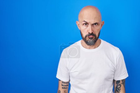 Téléchargez les photos : Homme hispanique avec des tatouages debout sur fond bleu déprimé et inquiet pour la détresse, pleurer en colère et peur. triste expression. - en image libre de droit