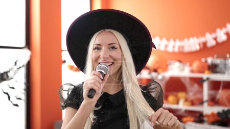 Photo for Young blonde woman wearing witch costume singing song at home - Royalty Free Image