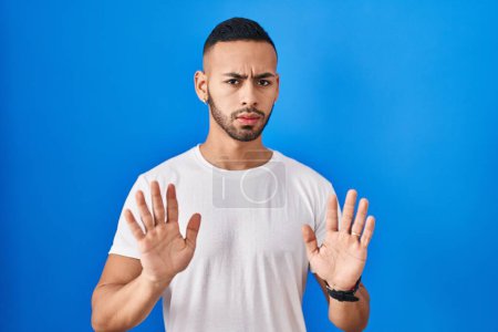 Photo for Young hispanic man standing over blue background moving away hands palms showing refusal and denial with afraid and disgusting expression. stop and forbidden. - Royalty Free Image