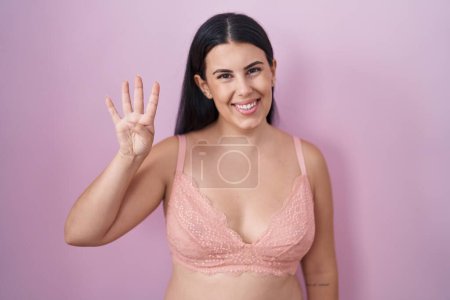 Téléchargez les photos : Jeune femme hispanique portant un soutien-gorge rose montrant et pointant vers le haut avec les doigts numéro quatre tout en souriant confiant et heureux. - en image libre de droit