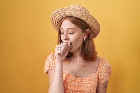 Téléchargez les photos : Jeune femme rousse debout sur fond jaune portant un chapeau d'été se sentant mal et toussant comme symptôme de rhume ou de bronchite. concept de soins de santé. - en image libre de droit