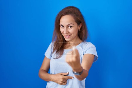 Photo for Brunette woman standing over blue background beckoning come here gesture with hand inviting welcoming happy and smiling - Royalty Free Image