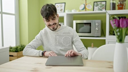 Téléchargez les photos : Jeune homme hispanique ouverture ordinateur portable à la salle à manger - en image libre de droit