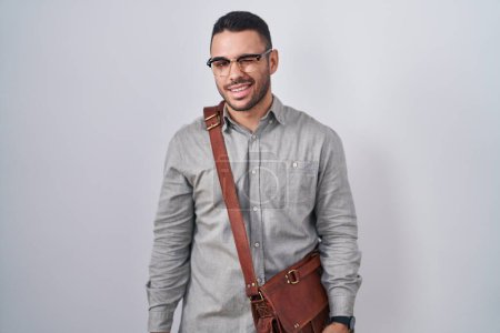 Téléchargez les photos : Jeune homme hispanique portant valise clin d'oeil en regardant la caméra avec une expression sexy, gai et heureux visage. - en image libre de droit